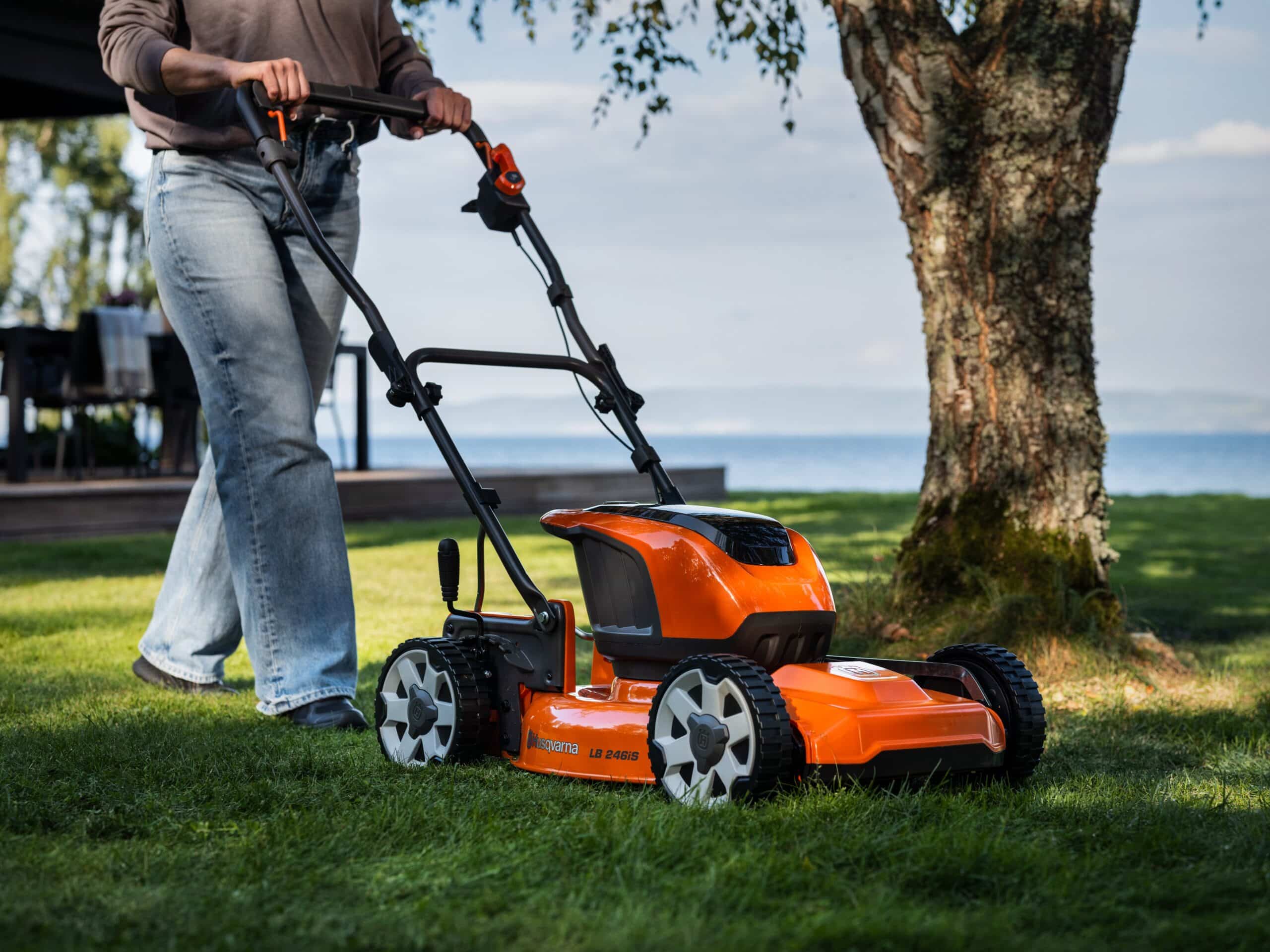 Person skubber en orange plæneklipper på en græsplæne.