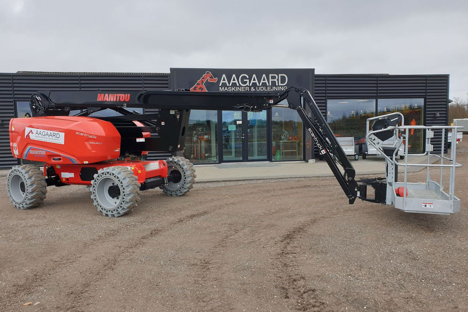Liftudlejning. En orange lift foran en bygning med Aagaard Maskiner & Udlejning-logoet.
