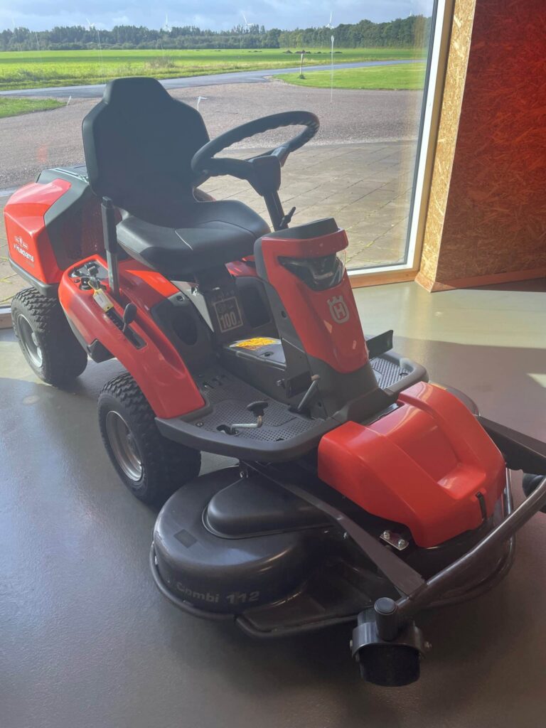 Rød plæneklipper udstillet indendørs foran et vindue.