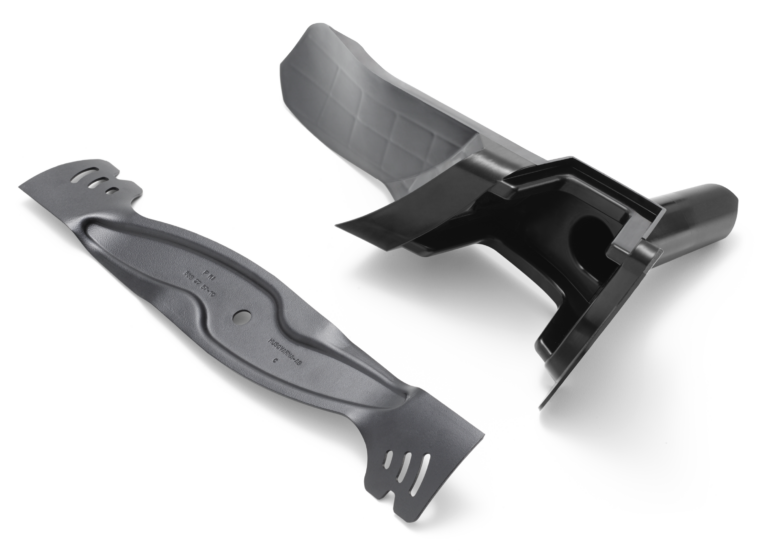 Et plæneklipperblad og et plasttilbehør på hvid baggrund.