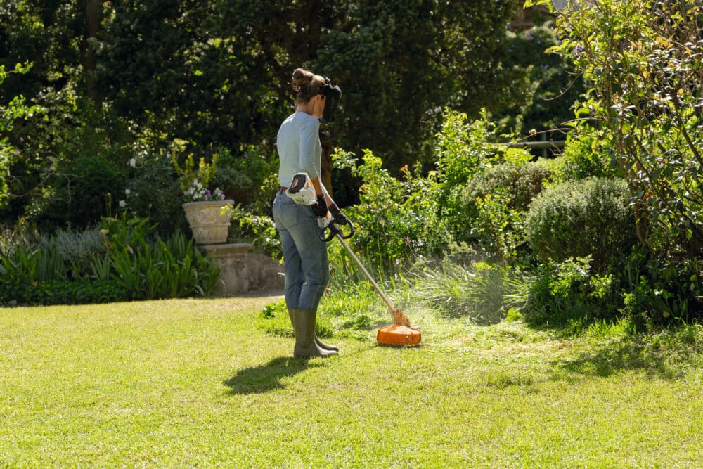 Person trimmer græs i en have med en orange trimmer