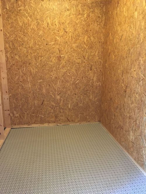 Et lille rum med vægge af OSB-plader og et mønstret gulv.