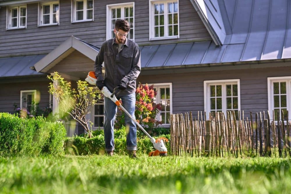 Mand bruger en græstrimmer i en have.