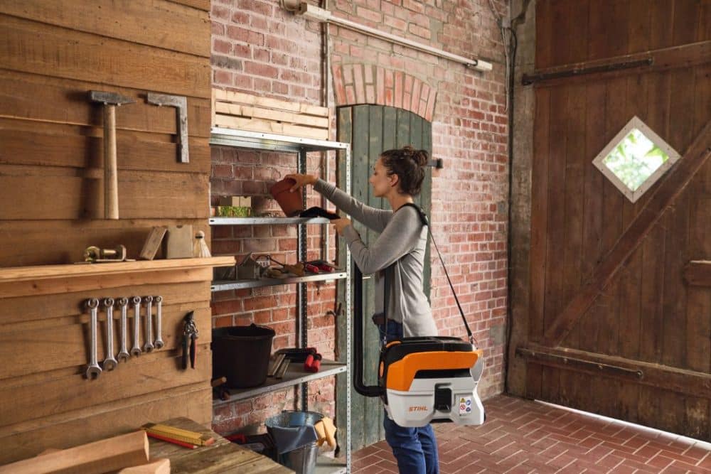 Kvinde står i værksted og rækker ud efter en plantepotte.