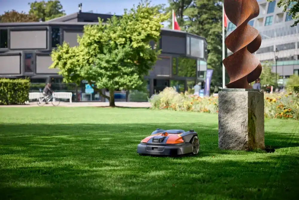 Robotplæneklipper kører på en græsplæne ved siden af en skulptur.