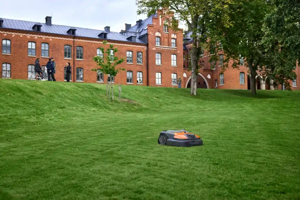 Robotgræsslåmaskine klipper græs foran en murstensbygning.