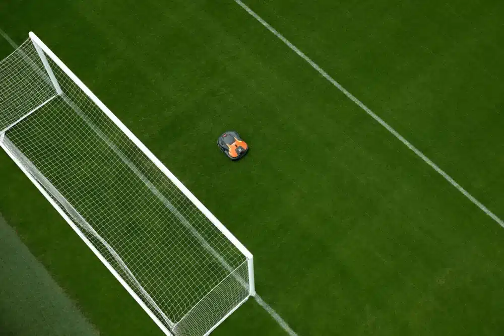Robotplæneklipper på en grøn græsplæne ved siden af et fodboldmål.
