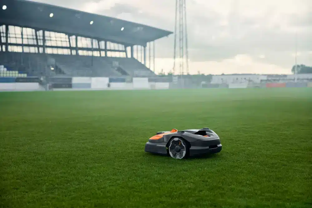 Robotplæneklipper på grøn fodboldbane foran tribune