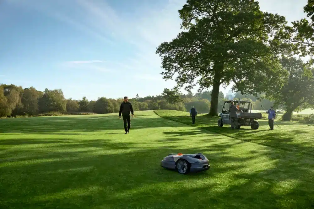 Robotplæneklipper på en golfbane med mennesker i baggrunden.