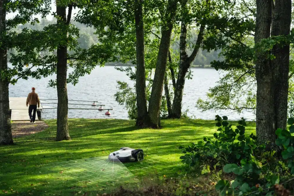 Robotplæneklipper på græsplæne nær sø.