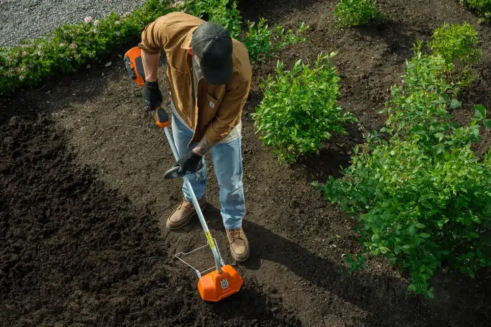 Mand bruger en orange jordfræser i en have