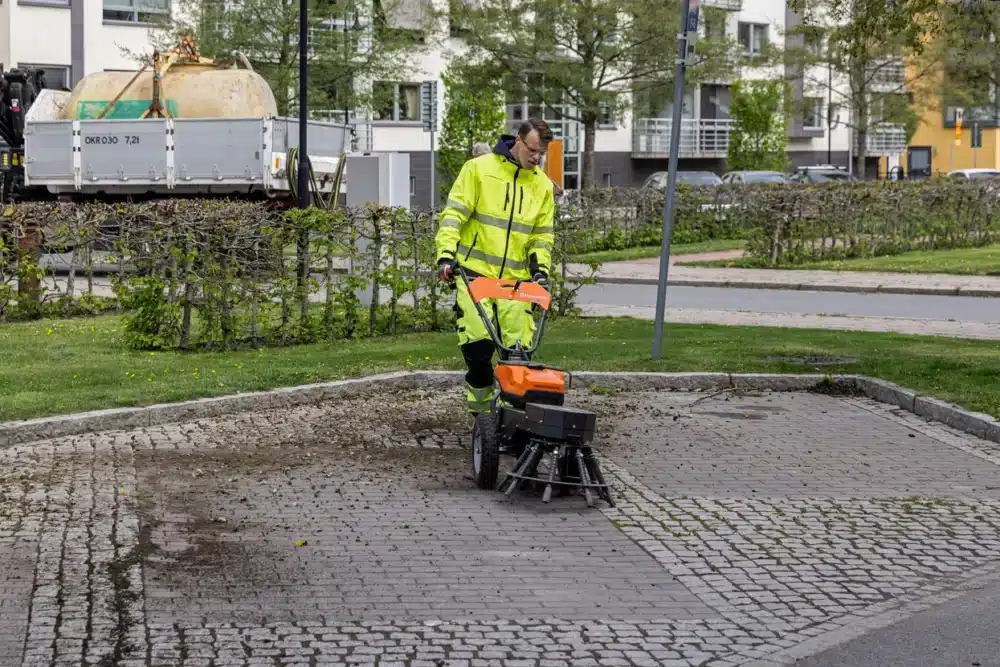 Mand i sikkerhedstøj betjener rengøringsmaskine på brosten