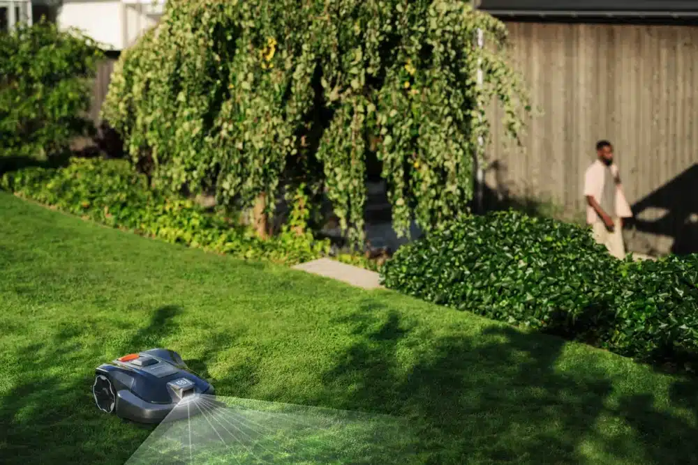 Robotplæneklipper på en græsplæne ved siden af en person.