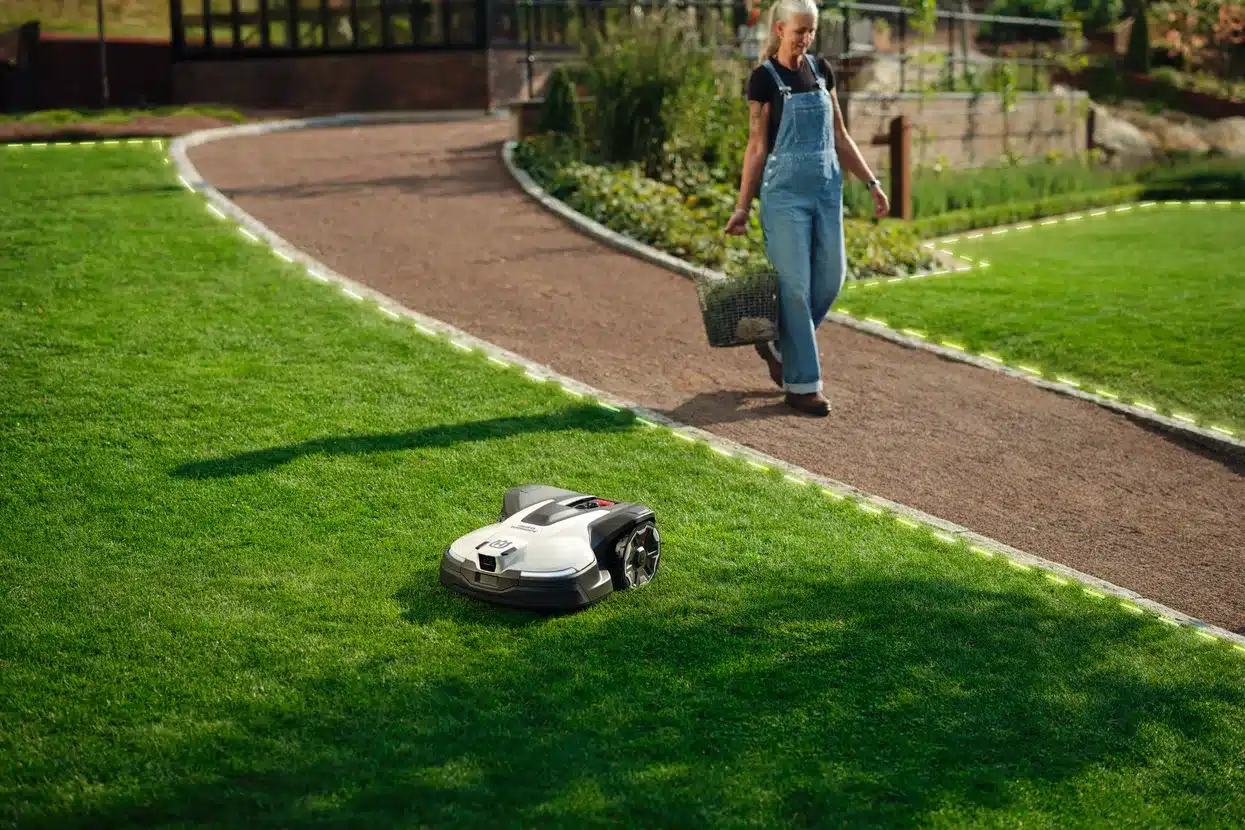 En robotplæneklipper kører på en velplejet græsplæne, mens en person går på stien.