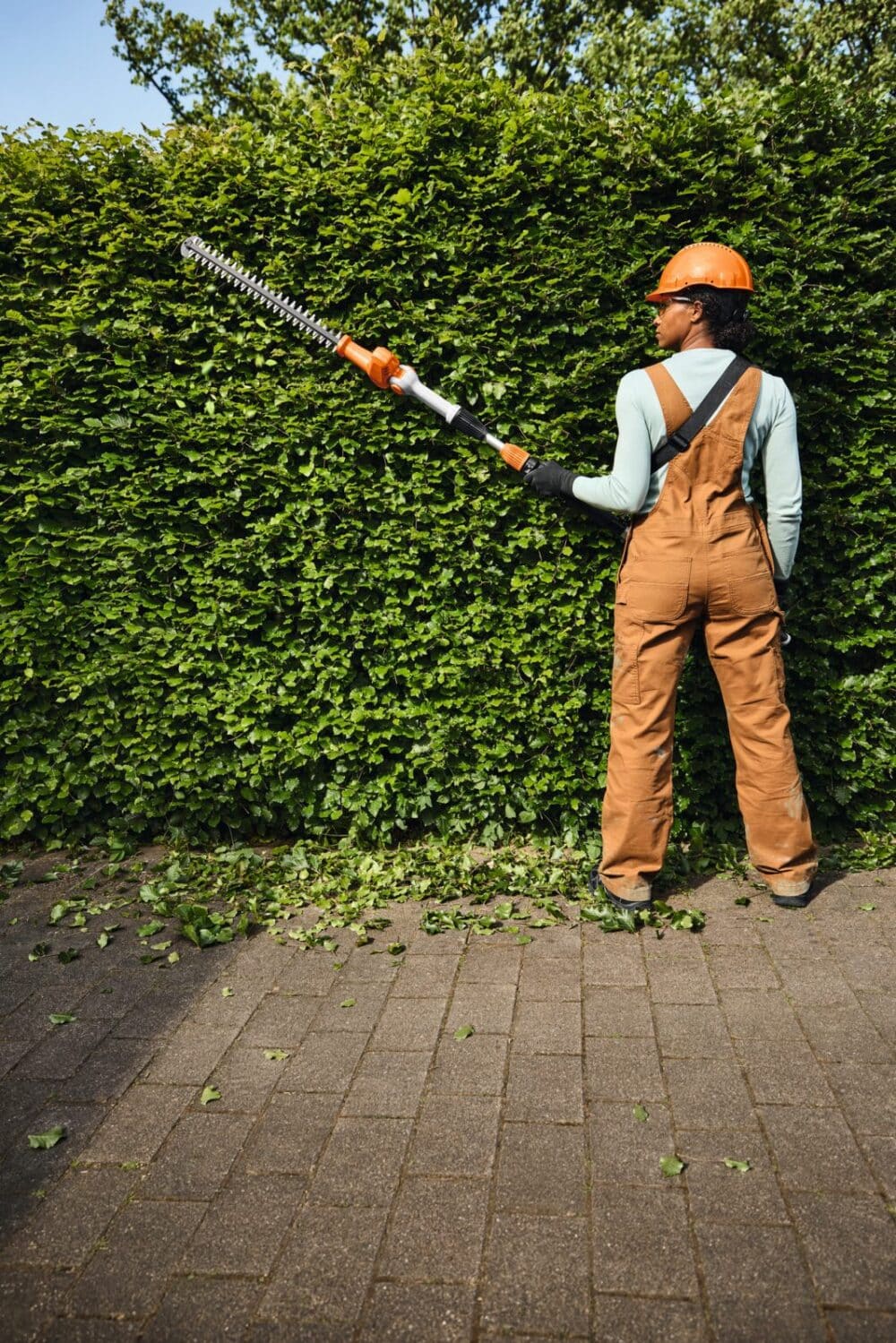 Person beskærer hæk med elektrisk trimmer