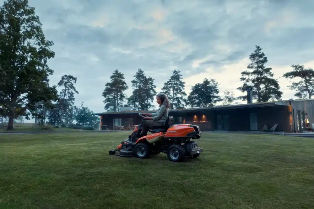 Kvinde på en orange havetraktor foran et moderne hus.