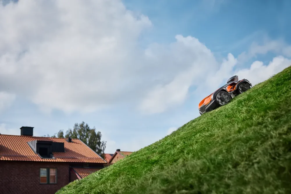 Robotplæneklipper kører op ad en græsskråning.