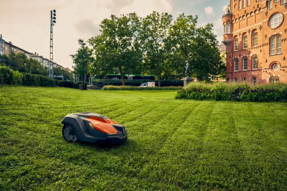 En robotplæneklipper på en grøn græsplæne ved siden af en bygning.