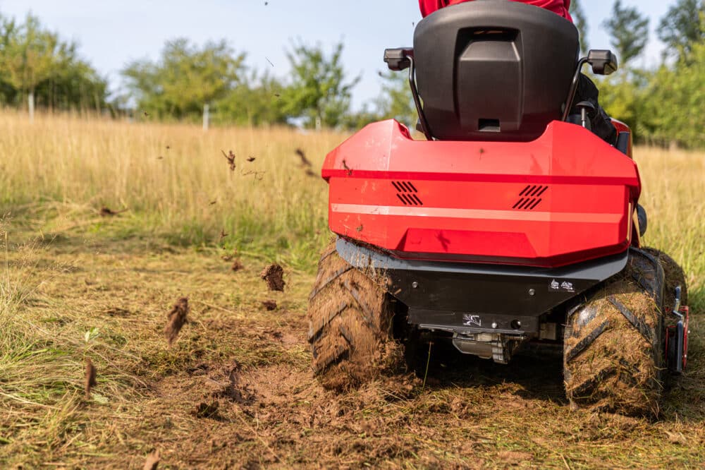 Rød græsslåmaskine kører gennem en mark og kaster jord op.