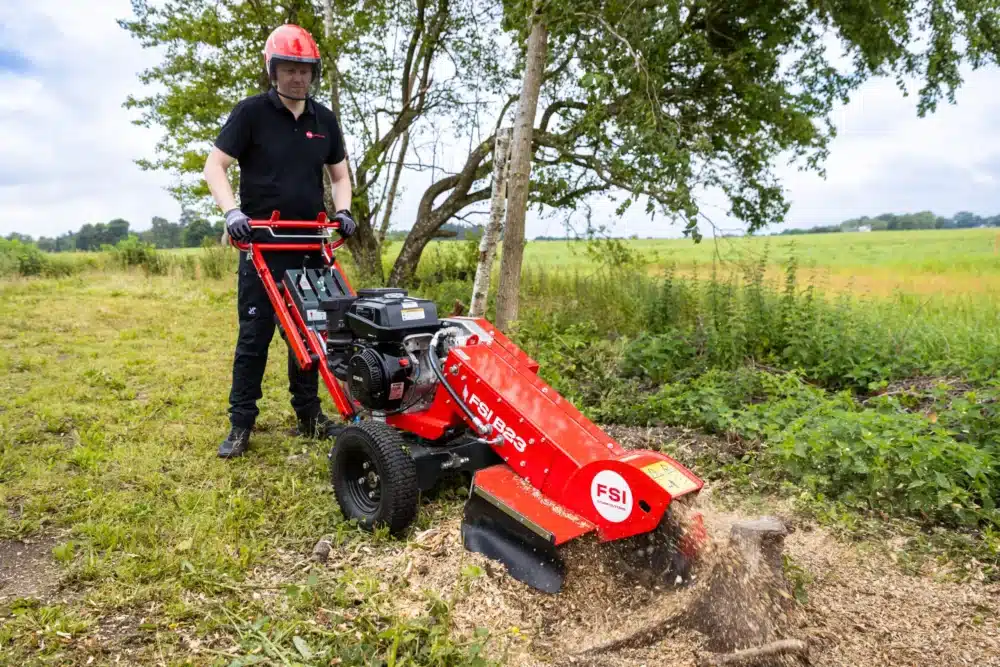 Mand bruger en rød stubfræser på en græsmark.
