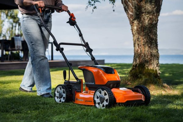 Person skubber en orange plæneklipper på en græsplæne.